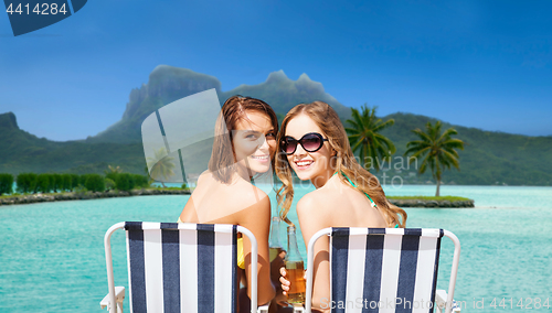 Image of happy young women with drinks sunbathing on beach