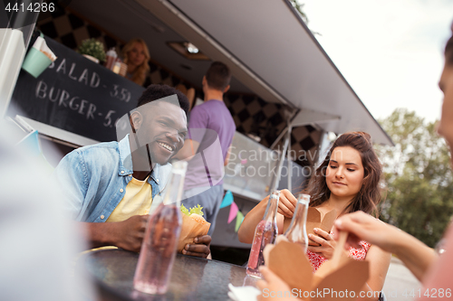 Image of happy friends with drinks eating at food truck