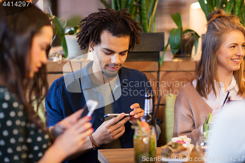 Image of friends with smartphones eating at restaurant