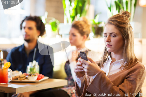 Image of woman with smartphone and friends at restaurant