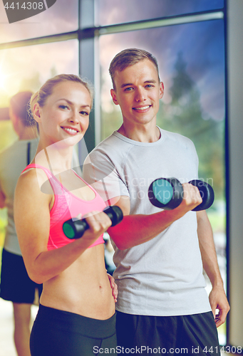 Image of smiling young woman with personal trainer in gym