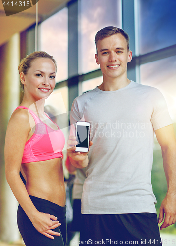 Image of smiling young woman with personal trainer in gym