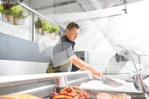 Image of male seller adding ice to fridge at fish shop