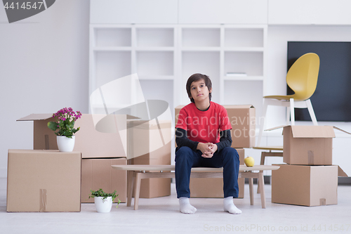 Image of boy sitting on the table with cardboard boxes around him