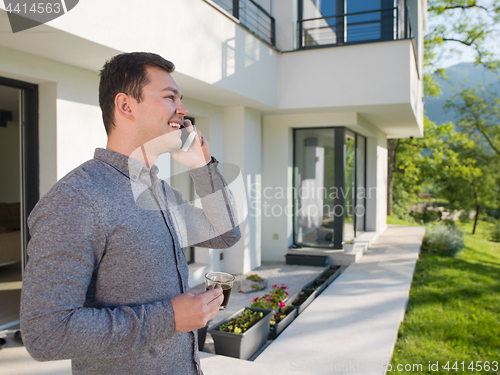 Image of man using mobile phone in front of his luxury home villa