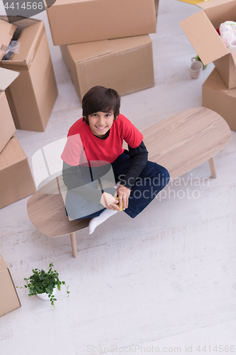 Image of boy sitting on the table with cardboard boxes around him top vie