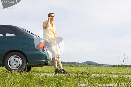Image of Man talking on cell phone beside his car