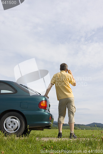 Image of Man talking on cell phone beside his car