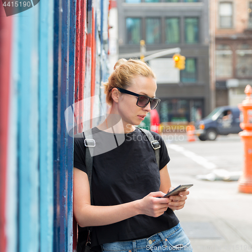 Image of Woman using smartphone against colorful graffiti wall in New York city, USA.