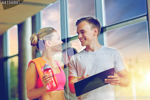 Image of smiling young woman with personal trainer in gym