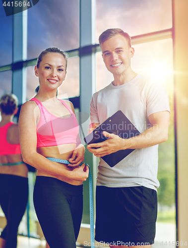 Image of smiling young woman with personal trainer in gym