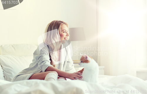 Image of happy young woman with cat in bed at home