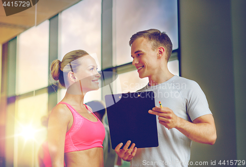 Image of smiling young woman with personal trainer in gym