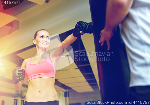 Image of smiling woman with personal trainer boxing in gym