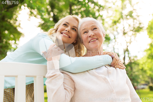 Image of daughter with senior mother hugging on park bench