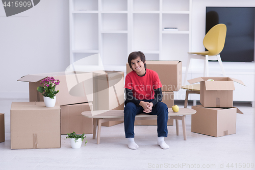 Image of boy sitting on the table with cardboard boxes around him