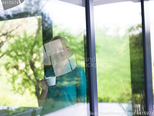 Image of young woman drinking morning coffee by the window