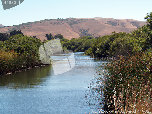 Image of waterway slough with hills grass reeds and blue sky