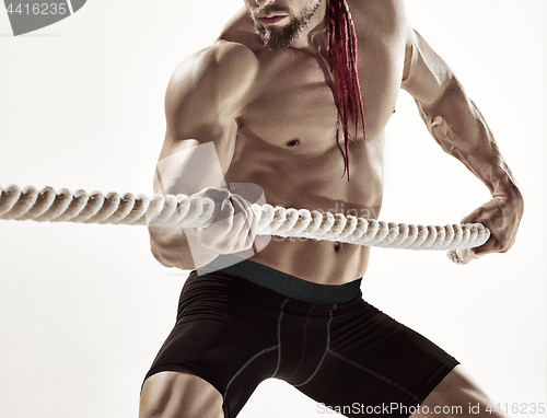 Image of Attractive muscular man working out with heavy ropes.