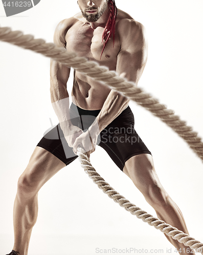 Image of Attractive muscular man working out with heavy ropes.