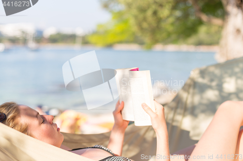 Image of Woman reading book in hammock on the beach