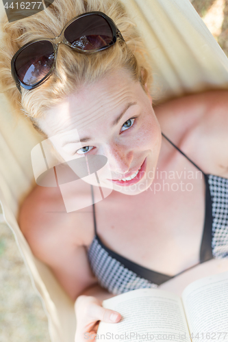 Image of Woman reading book in hammock on the beach