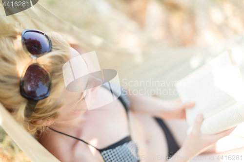 Image of Woman reading book in hammock on the beach