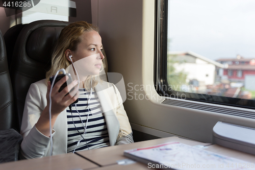Image of Thoughtful businesswoman listening to podcast on mobile phone while traveling by train.