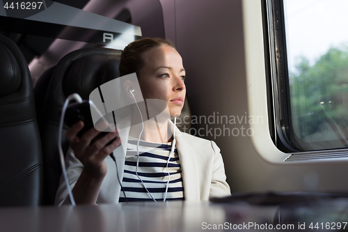 Image of Thoughtful businesswoman listening to podcast on mobile phone while traveling by train.