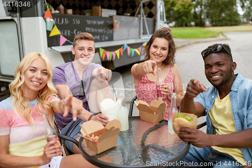 Image of happy friends with drinks eating at food truck