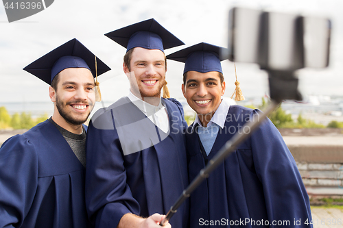 Image of happy male students taking picture by selfie stick