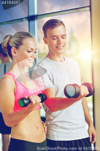 Image of smiling young woman with personal trainer in gym