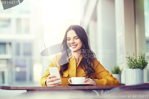 Image of happy woman texting on smartphone at city cafe