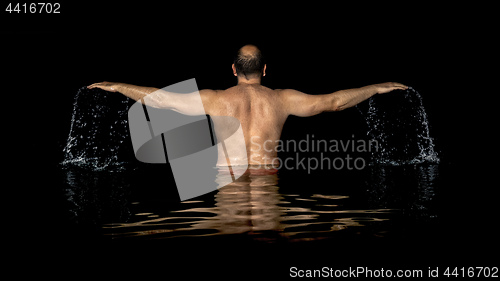 Image of A man standing inside the water and spreads his arms