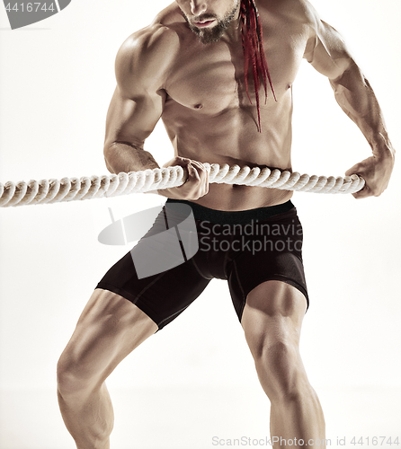 Image of Attractive muscular man working out with heavy ropes.