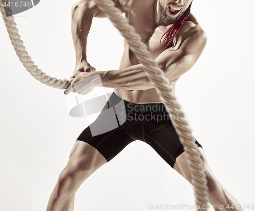 Image of Attractive muscular man working out with heavy ropes.