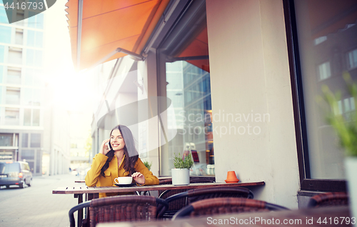 Image of happy woman calling on smartphone at city cafe