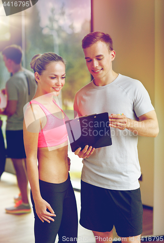 Image of smiling young woman with personal trainer in gym