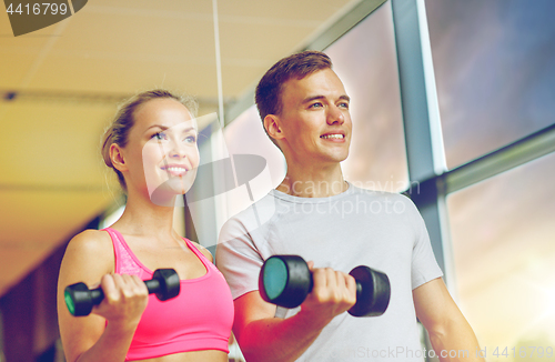 Image of smiling young woman with personal trainer in gym