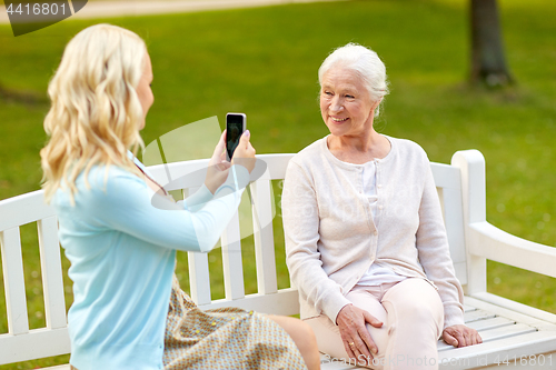 Image of daughter photographing senior mother by smartphone