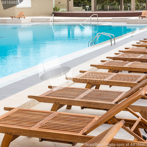 Image of Luxury swimming pool with wooden deck chairs.