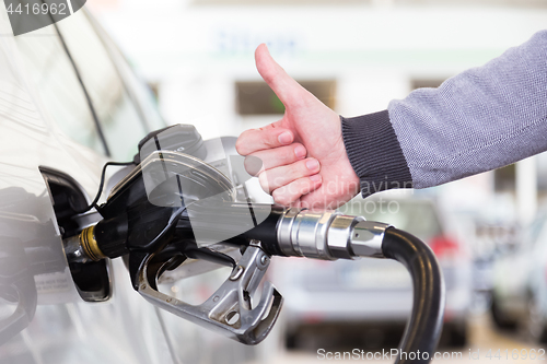 Image of Petrol or gasoline being pumped into a motor vehicle car. Closeup of man, showing thumb up gesture, pumping gasoline fuel in car at gas station.