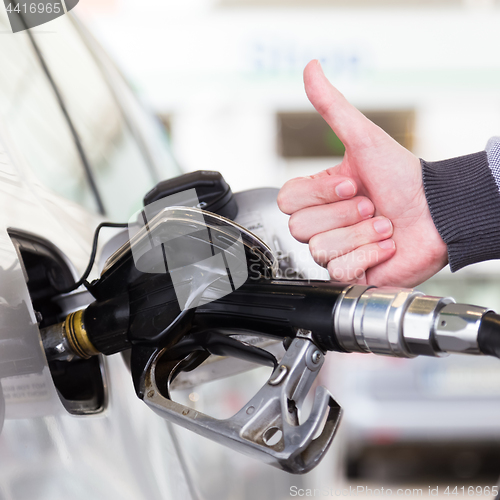 Image of Petrol or gasoline being pumped into a motor vehicle car. Closeup of man, showing thumb up gesture, pumping gasoline fuel in car at gas station.