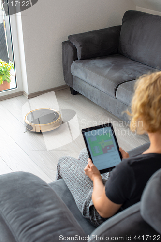 Image of Woman is steering her vacuum cleaning robot from the sofa