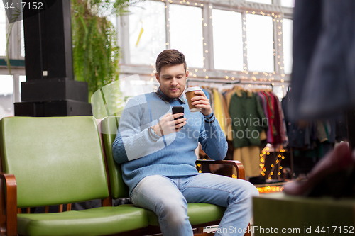 Image of man with smartphone and coffee at clothing store