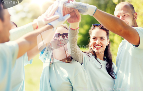 Image of group of happy volunteers making high five in park