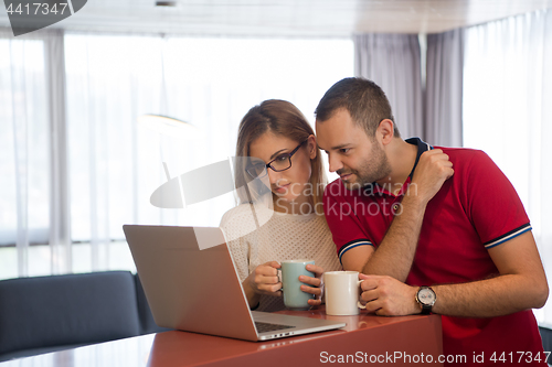 Image of couple drinking coffee and using laptop at home