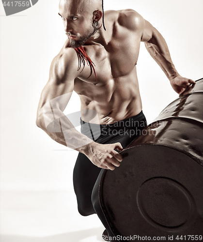 Image of Fitness man with perfect body doing exercises with iron barrel