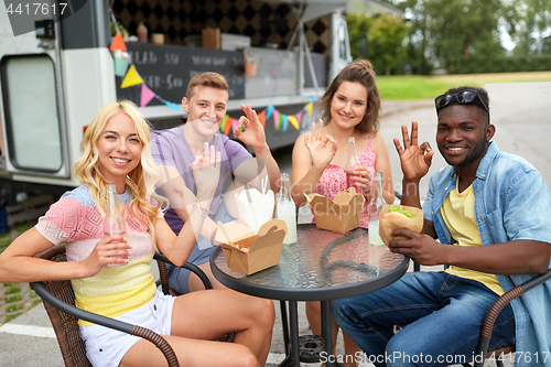 Image of happy friends with drinks eating at food truck