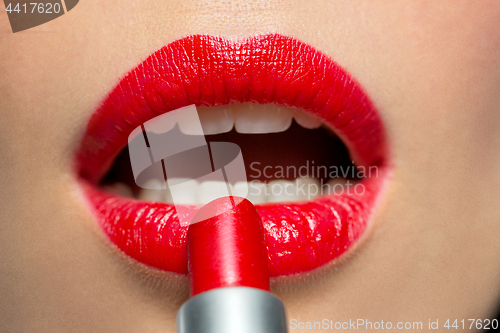 Image of close up of woman applying red lipstick to lips